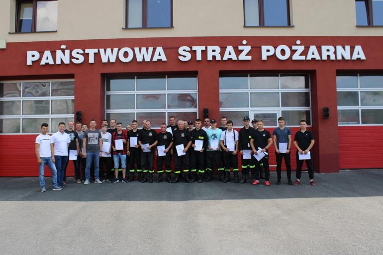 Druhowie przed garażem Jednostki Ratowniczo Gaśniczej Komendy Powiatowej PSP w Janowie Lubelskim z zaświadczeniami potwierdzającymi ukończenie kursu