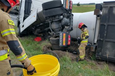 Strażacy przepompowują rozlany olej napędowy z uszkodzonego zbiornika ciągnika siodłowego do zastępczego pojemnika dostarczonego przez D-cę JRG