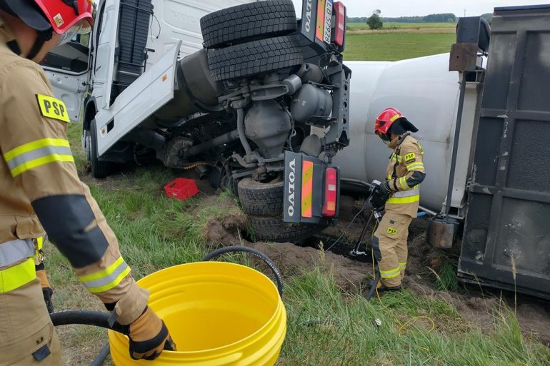 Strażacy przepompowują rozlany olej napędowy z uszkodzonego zbiornika ciągnika siodłowego do zastępczego pojemnika dostarczonego przez D-cę JRG