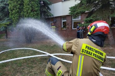 Strażacy z linią gaśniczą prezentują gaszenie pożaru przy oknach Uniwersyteckiego Szpitala Dziecięcego w Lublinie