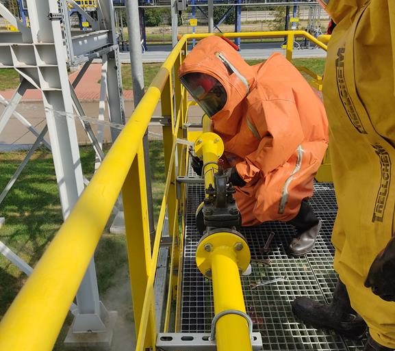Strażacy ze Specjalistycznej Grupy Chemicznej PSP w kombinezonach gazoszczelnych usuwają wyciech z instalacji przesyłowej ciekłego amoniaku