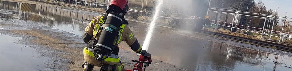 Strażak przy użyciu działka wodnego schładza płaszcz palącej się cysterny z gazem