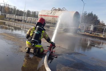 Strażak przy użyciu działka wodnego schładza płaszcz palącej się cysterny z gazem