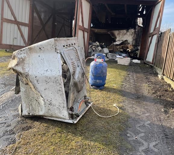 Rumowisko budynków gospodarczych po wybuchu gazu. Na pierwszym planie zniszczona kuchenka gazowa i butla