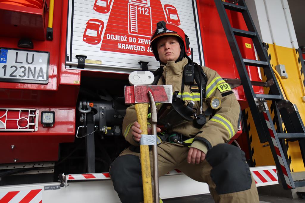Strażak prezentuje czujnik tlenku węgla na tle samochodu pożarniczego